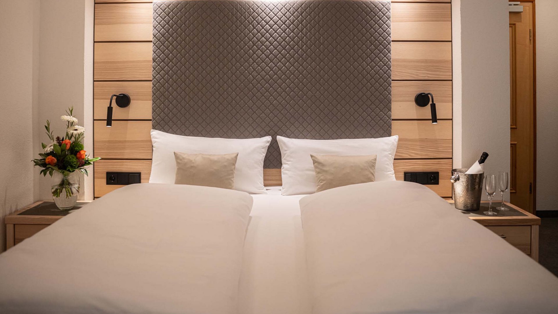 Das Hotel Filser, Ihr Hotel in Oberstdorf im Allgäu Modernes Hotelzimmer mit Doppelbett, Leselampen und Blumenvasen